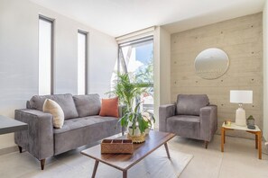 Ein modernes Wohnzimmer mit zwei grauen Sofas, einem Holztisch, einer Topfpflanze und einem runden Spiegel an der Wand.