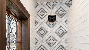 Un baño con paredes de azulejos blancos, un diseño geométrico, una ventana con marco de madera y una ducha con panel de control negro.