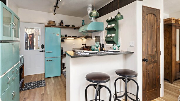 Una cocina con un refrigerador azul, armarios de madera y una zona con taburete de bar.