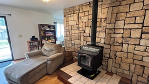 A living room with a stone wall, a fireplace labeled 'Lake Almanor', a sofa, and a bookshelf. - Cozy 3BR Home in Chester Near Lake Almanor and Mt Lassen (Chester)