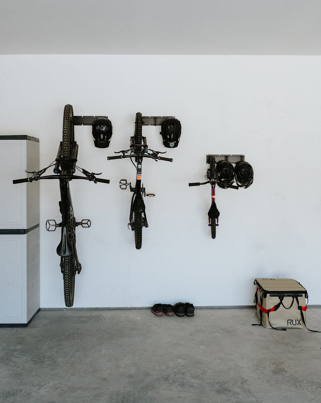 Una habitación con tres bicicletas colgadas en la pared, un par de zapatos en el suelo y una caja de cartón con la etiqueta "ROX" a la derecha.