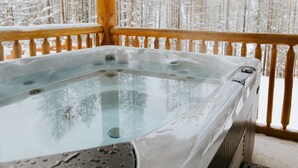 Ein Whirlpool auf einer Holzterrasse mit verschneitem Wald im Hintergrund.