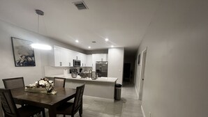 A modern kitchen with white cabinets, a stainless steel refrigerator, and a dining area with a dark wooden table and chairs.