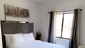 A modern bedroom with a large bed, a ceiling fan, a window with curtains, and a wall-mounted artwork.