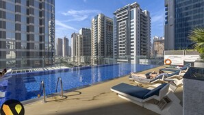 Un área de piscina en la azotea con sillones y vistas a edificios altos circundantes.