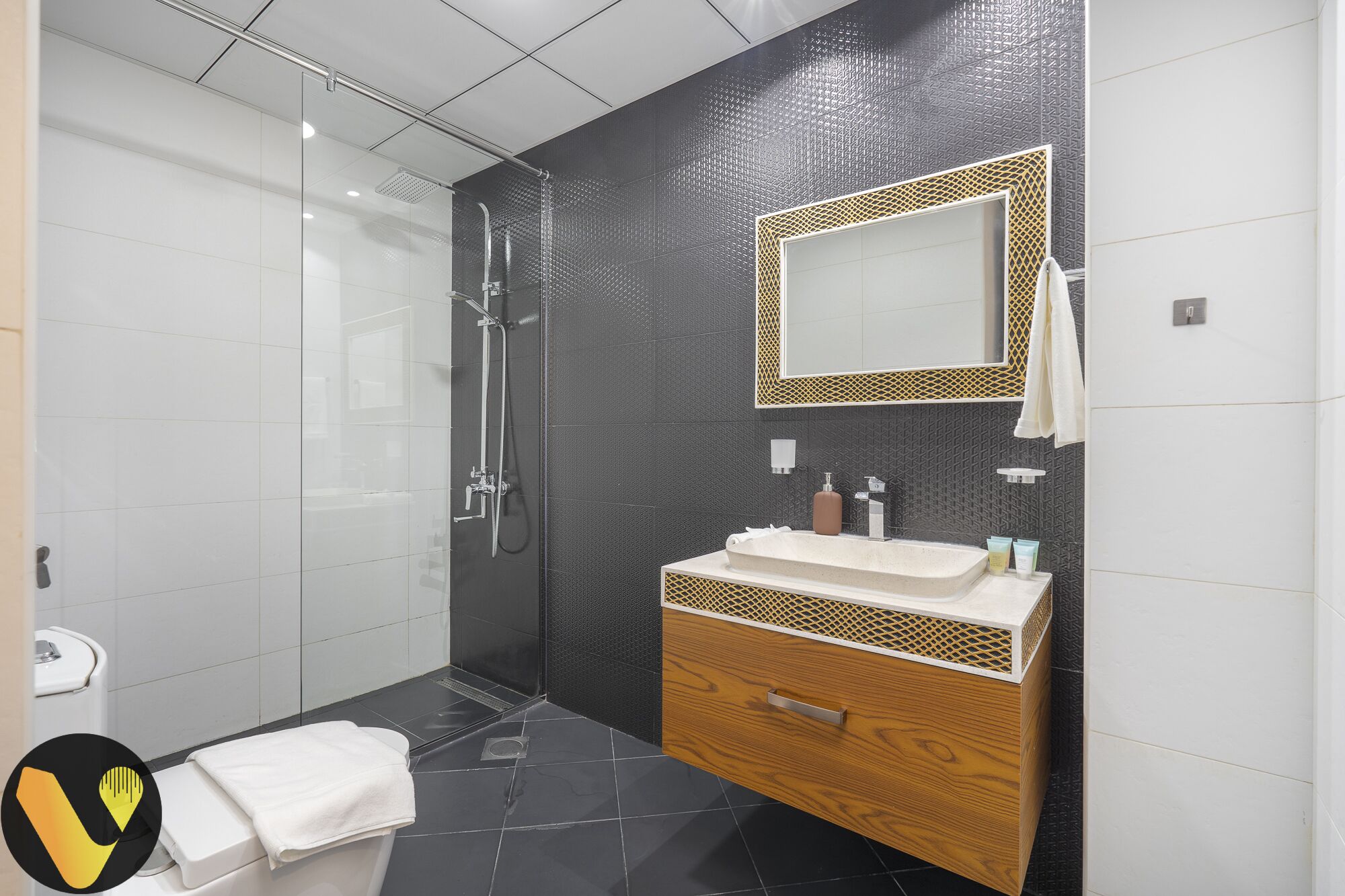 A modern bathroom with a glass shower enclosure, a wooden vanity with a white sink, and a large mirror with a decorative frame.