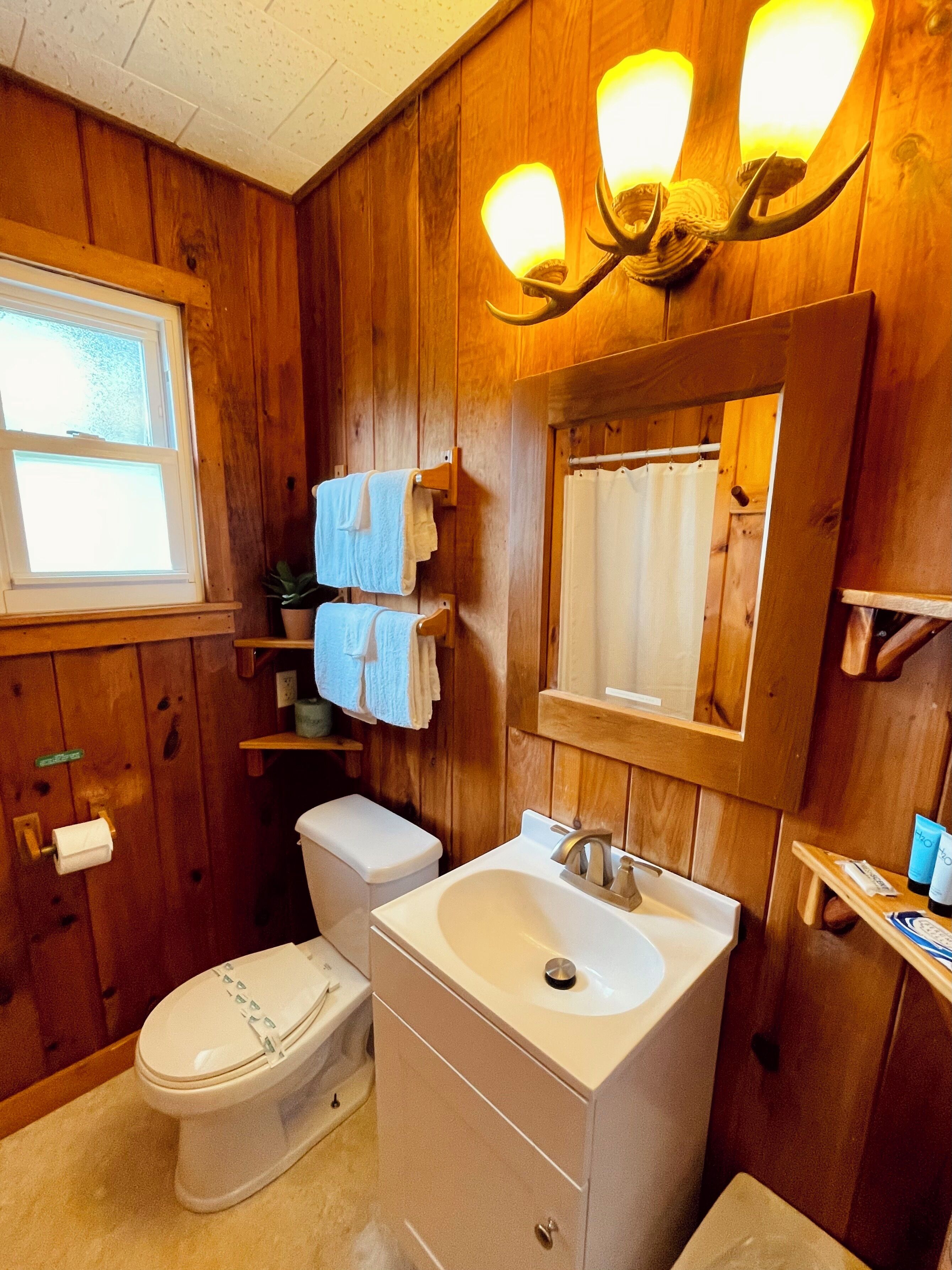 A wooden-paneled bathroom with a toilet, sink, and two towel racks.
