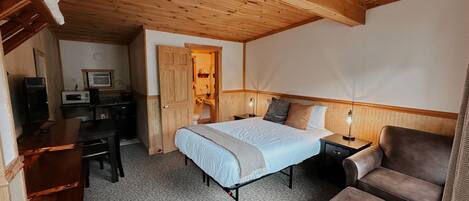 Un dormitorio con cama, escritorio, silla y baño visible a través de una puerta abierta.
