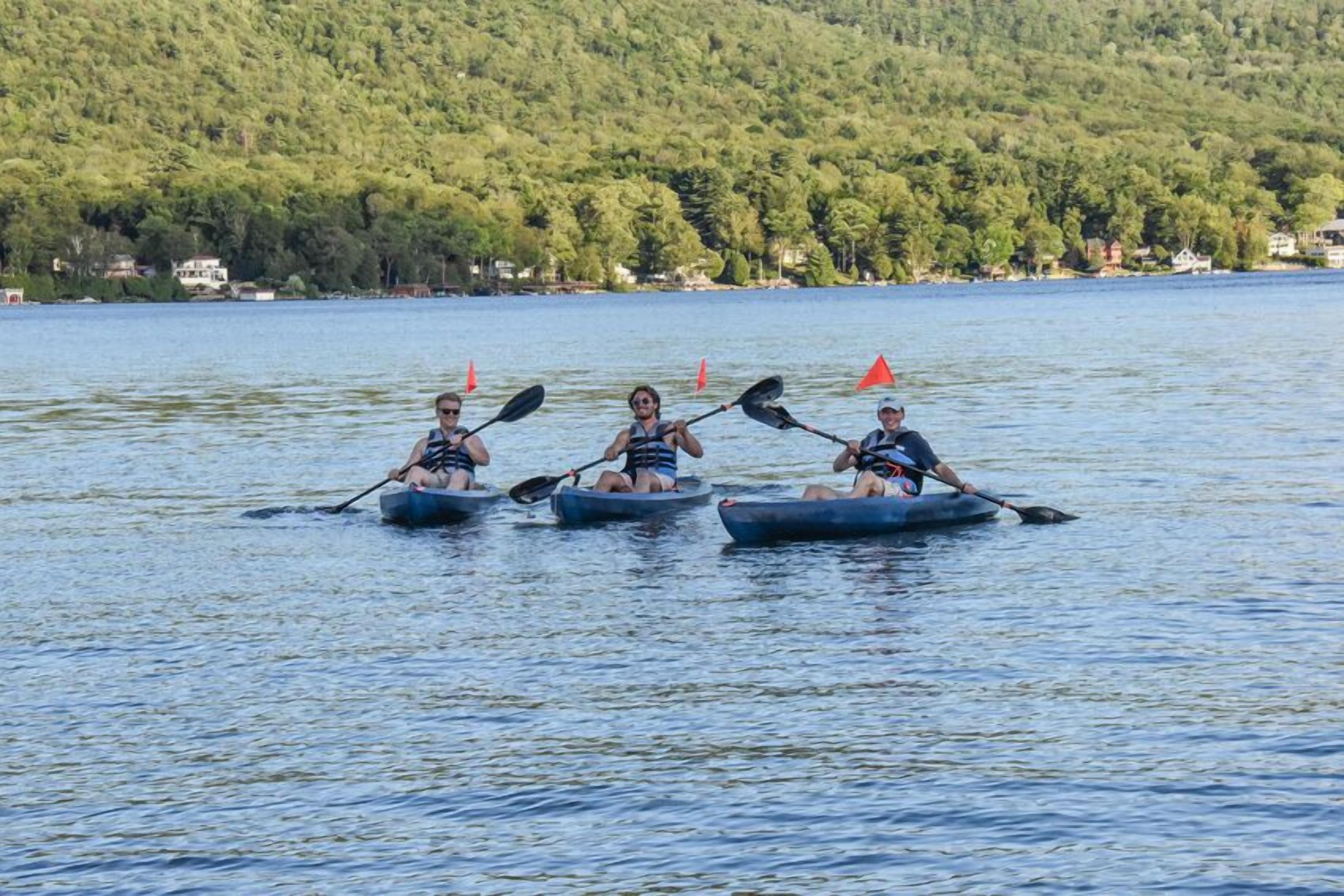 Three kayaks on a calm lake with a forested hillside in the background.
