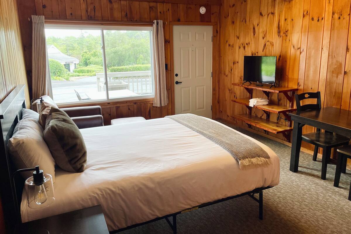 A wooden room with a bed, a television on a wooden stand, and a window with curtains.