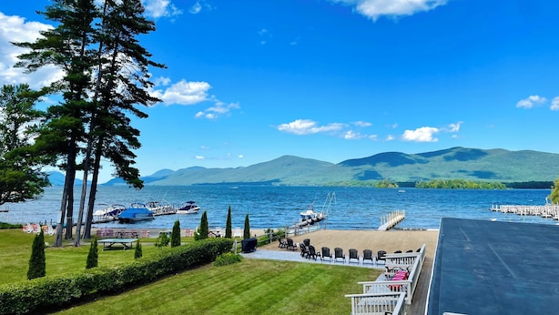 A lakeside view with boats docked, a deck with chairs and tables, and a mountain backdrop. - Waters Edge Lodge (Diamond Point)