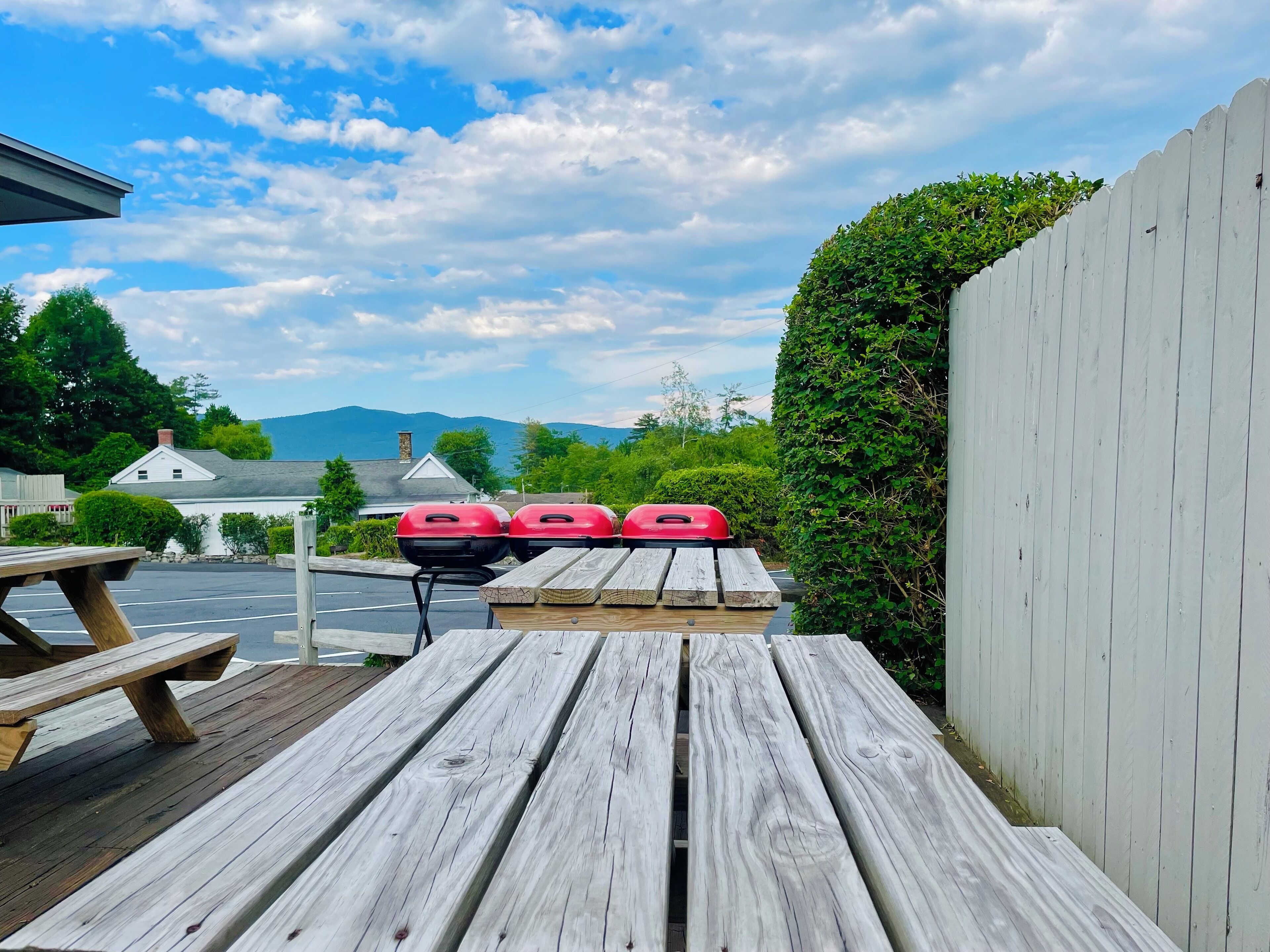 Een houten terras met picknicktafels en een barbecue.