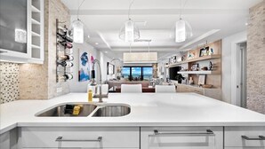 Une cuisine moderne dotée d’un grand îlot central, de meubles blancs et de luminaires suspendus.