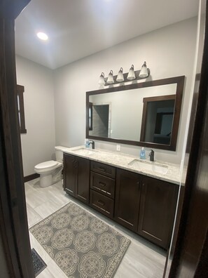 A bathroom with a large mirror, two sinks, a toilet, and a patterned rug.