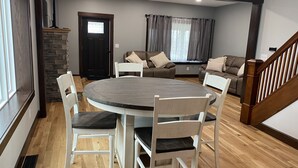 Een eetgedeelte met een ronde tafel en witte stoelen, een accentmuur van steen, en een trap.