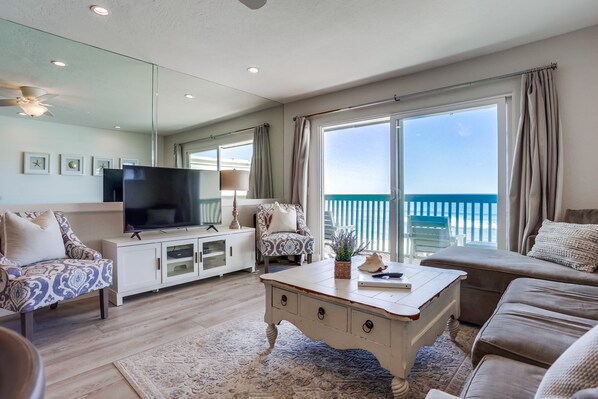 A spacious living room with a large flat-screen TV, comfortable seating, a coffee table, and a view of the ocean through large windows. - Beachfront Family Dream! On the strand in Oceanside - Pet friendly! (Oceanside)