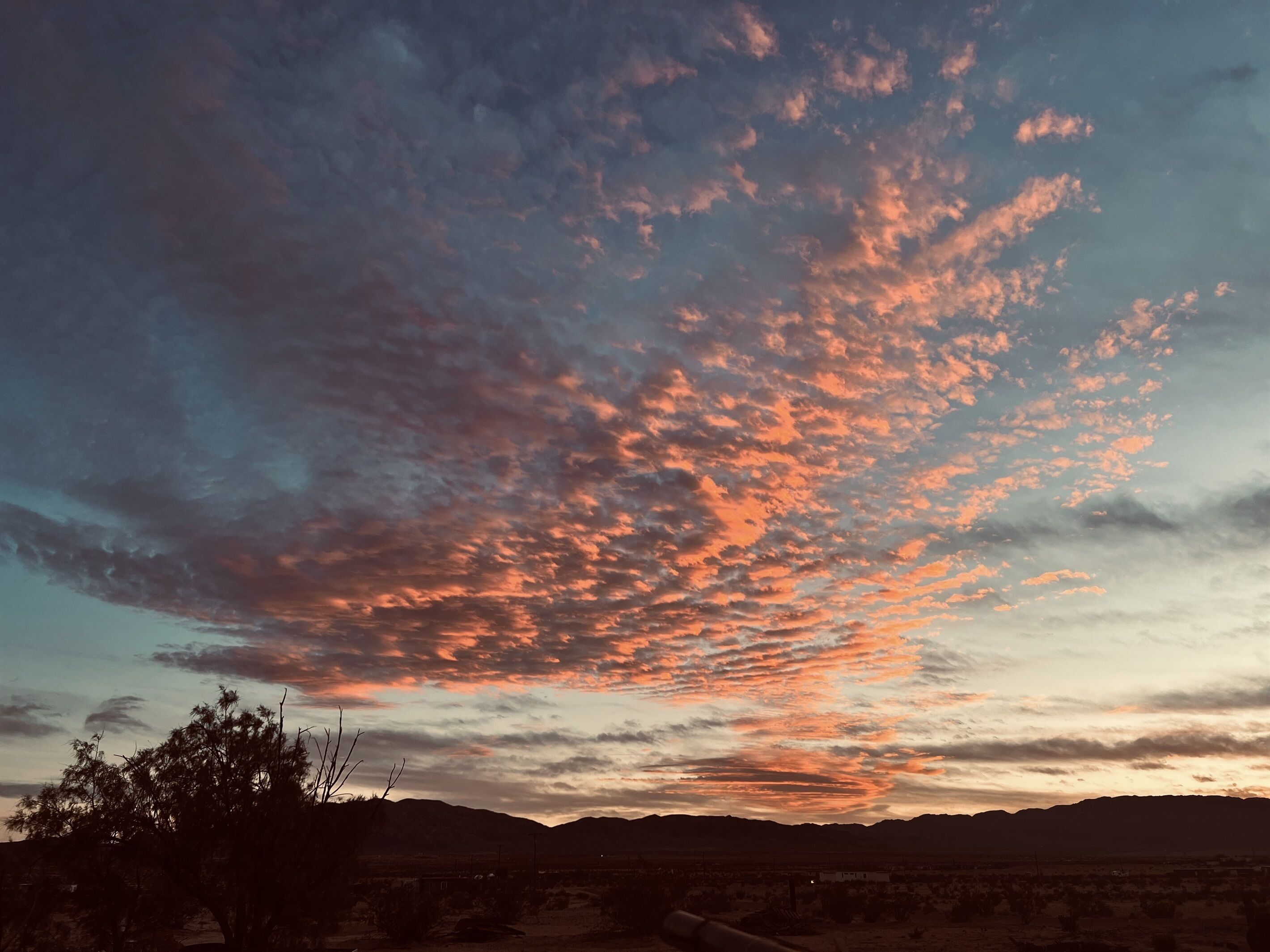 Un coucher de soleil sur un paysage désertique, avec des montagnes à l'horizon.