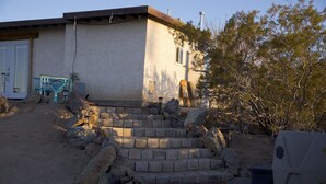 Una casa con una escalera de piedra que lleva a una puerta, rodeada de rocas y vegetación escasa.