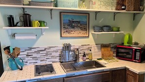 Una cocina con un lavaplatos doble, un microondas y diversos utensilios y electrodomésticos.