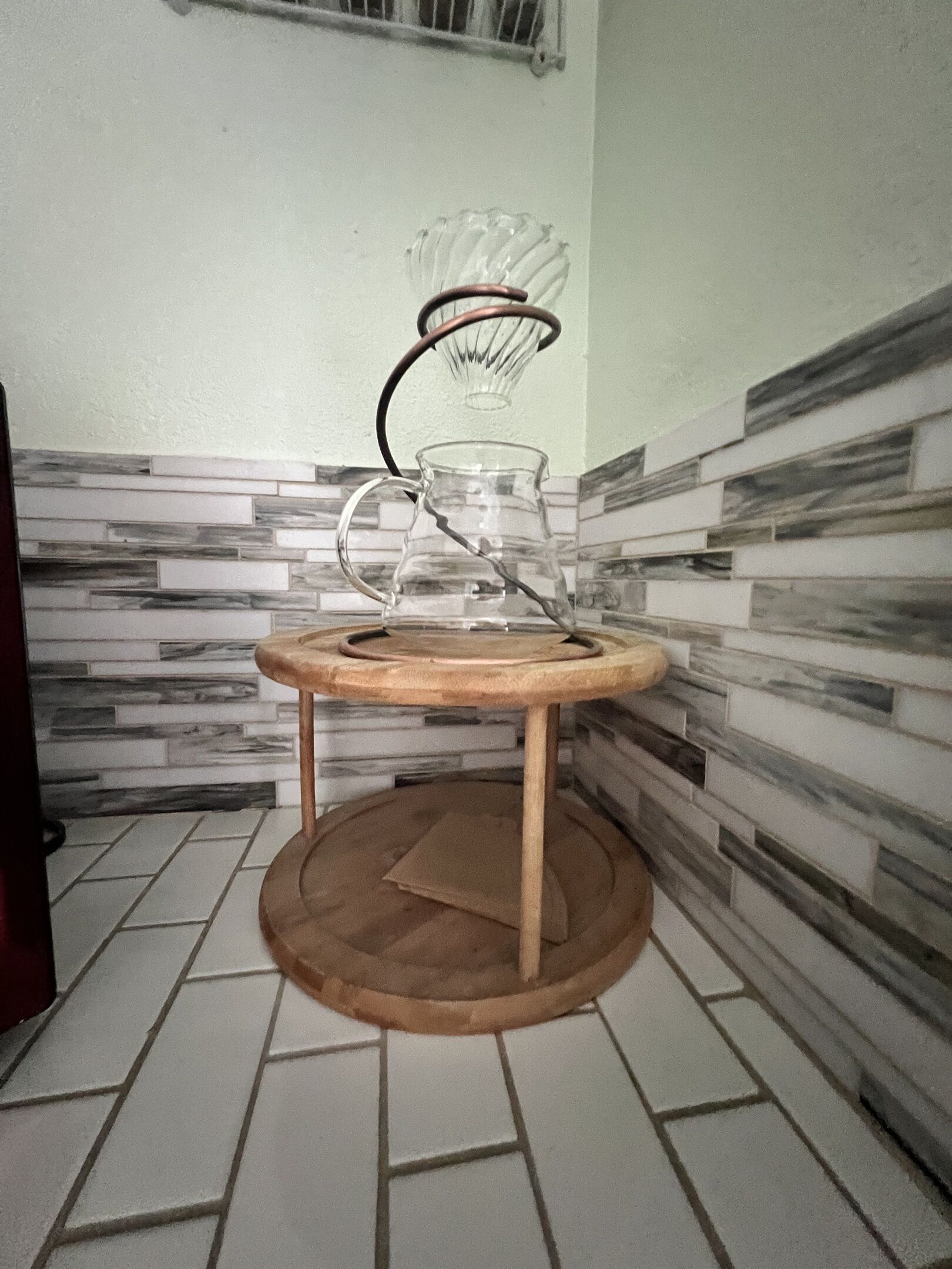 Eine Küche mit Fliesenboden, einem Holzschemel und einem Glasbehälter auf einem Metallständer.