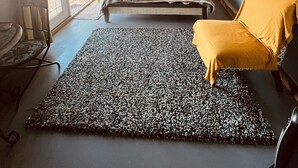 Un dormitorio con cama, ventilador de techo, alfombra estampada, una silla amarilla y una ventana con cortinas.