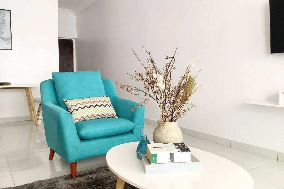 A modern living room with a teal armchair, a white coffee table, and a vase with dried branches.