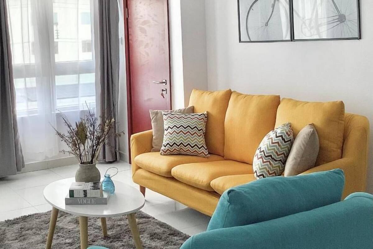 A modern living room with a yellow sofa, a small round coffee table, and a large window with curtains.