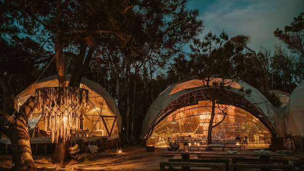 A series of dome-shaped tents with interior lighting, surrounded by trees. - Big Bang Nature Stays (Sauce de Portezuelo)