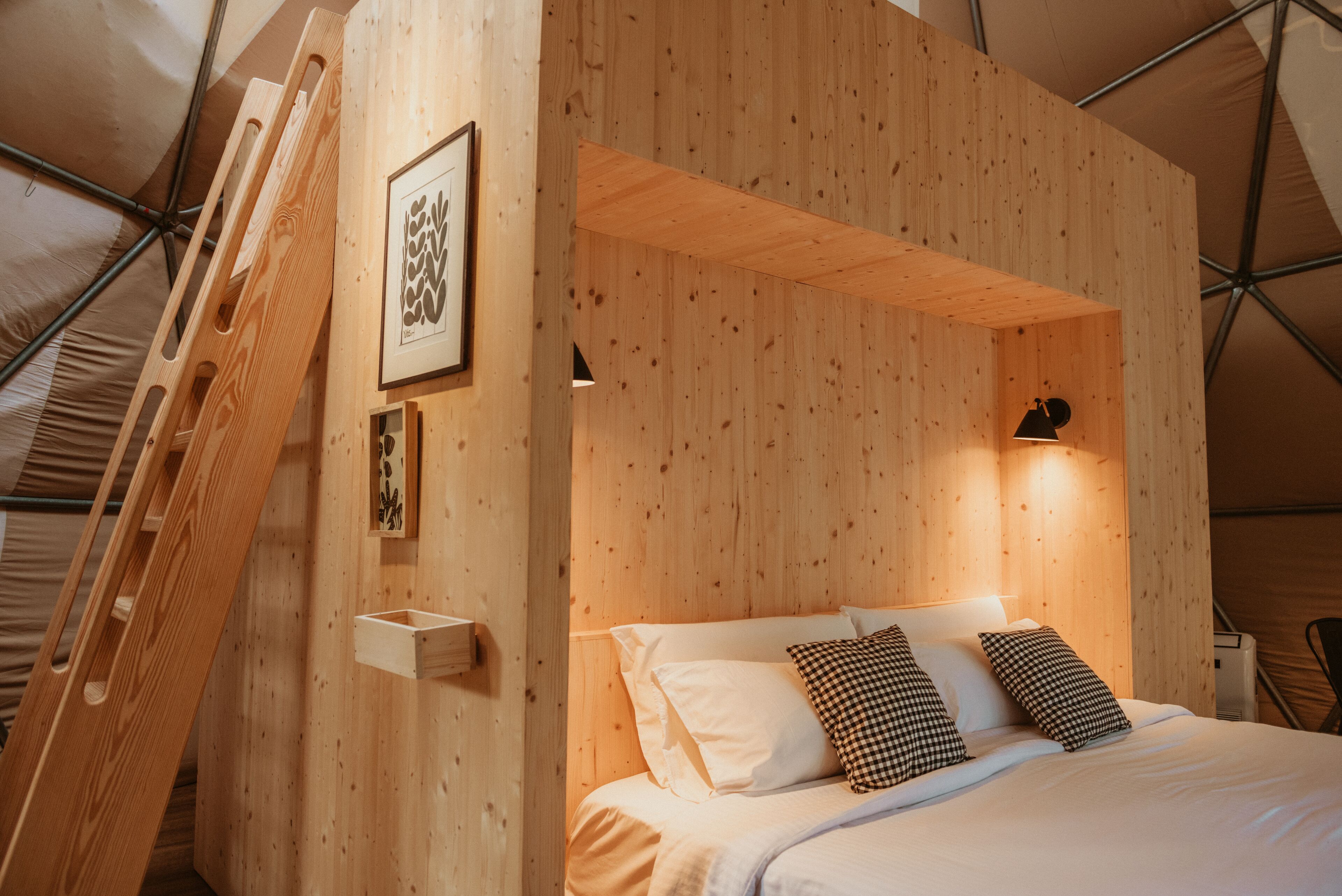 A wooden bunk bed with a ladder, a framed artwork, and a bedside table.