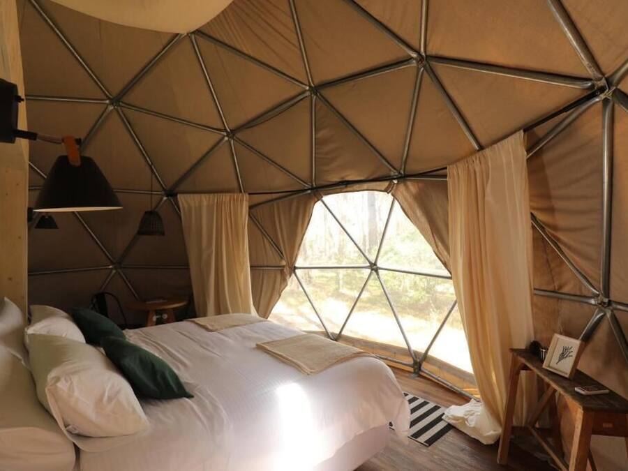 Una carpa acogedora y bien iluminada con una cama, una lámpara colgante y una ventana con cortinas.