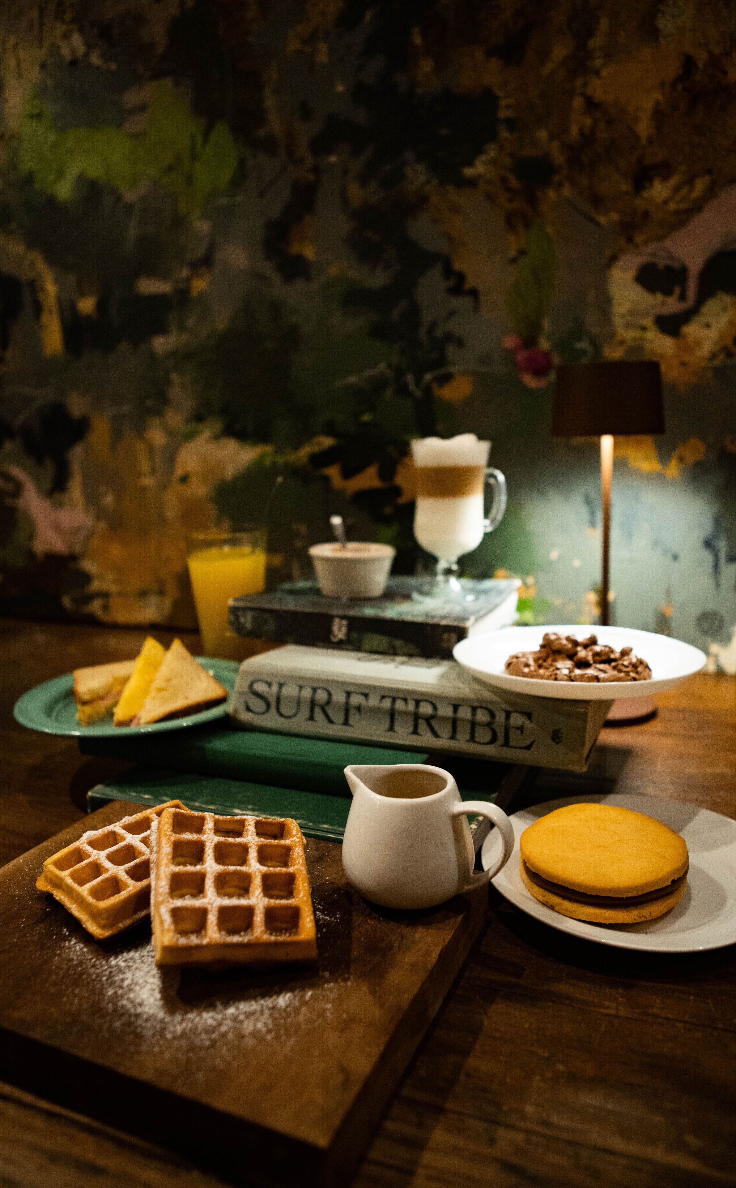 Una mesa con gofres, un sándwich, una taza de café y un libro titulado 'SURF TRIBE'.