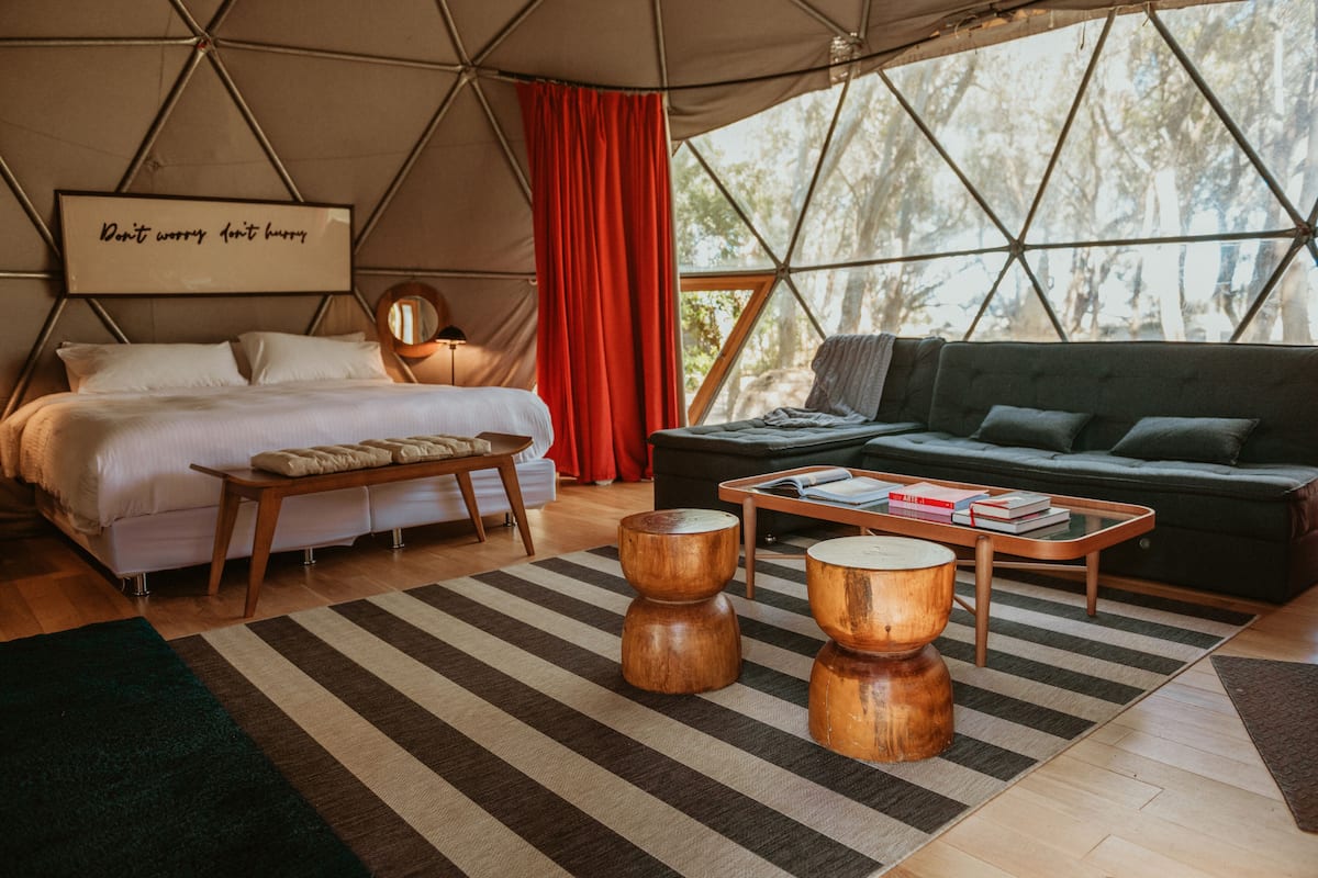 A cozy, well-lit tented accommodation with a bed, sofa, and wooden coffee table, featuring a motivational quote on the wall.