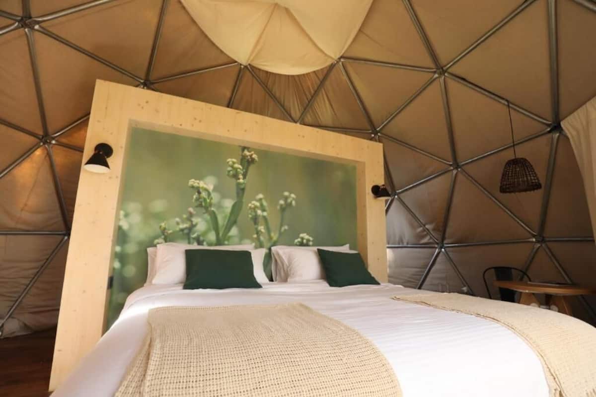 A tented accommodation room with a bed, pillows, and a wall-mounted lamp.