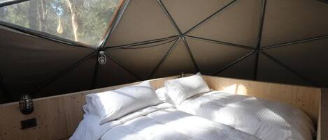 A cozy bedroom with a wooden bed, a window, and a tent-like ceiling structure.