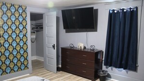 Ein Schlafzimmer mit einem Bett, einem Schminktisch, einem Fernseher, einer Tür und einem Vorhang.