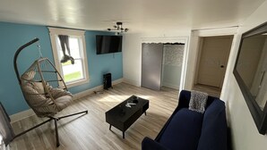Ein Wohnzimmer mit Hängekorbschaukel, Sofa, Couchtisch, Fernseher und Schiebetürenschrank.