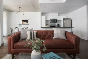 Un salon moderne avec un canapé marron, une table basse sur laquelle se trouvent un livre et un vase, et un coin repas avec des chaises et une table.