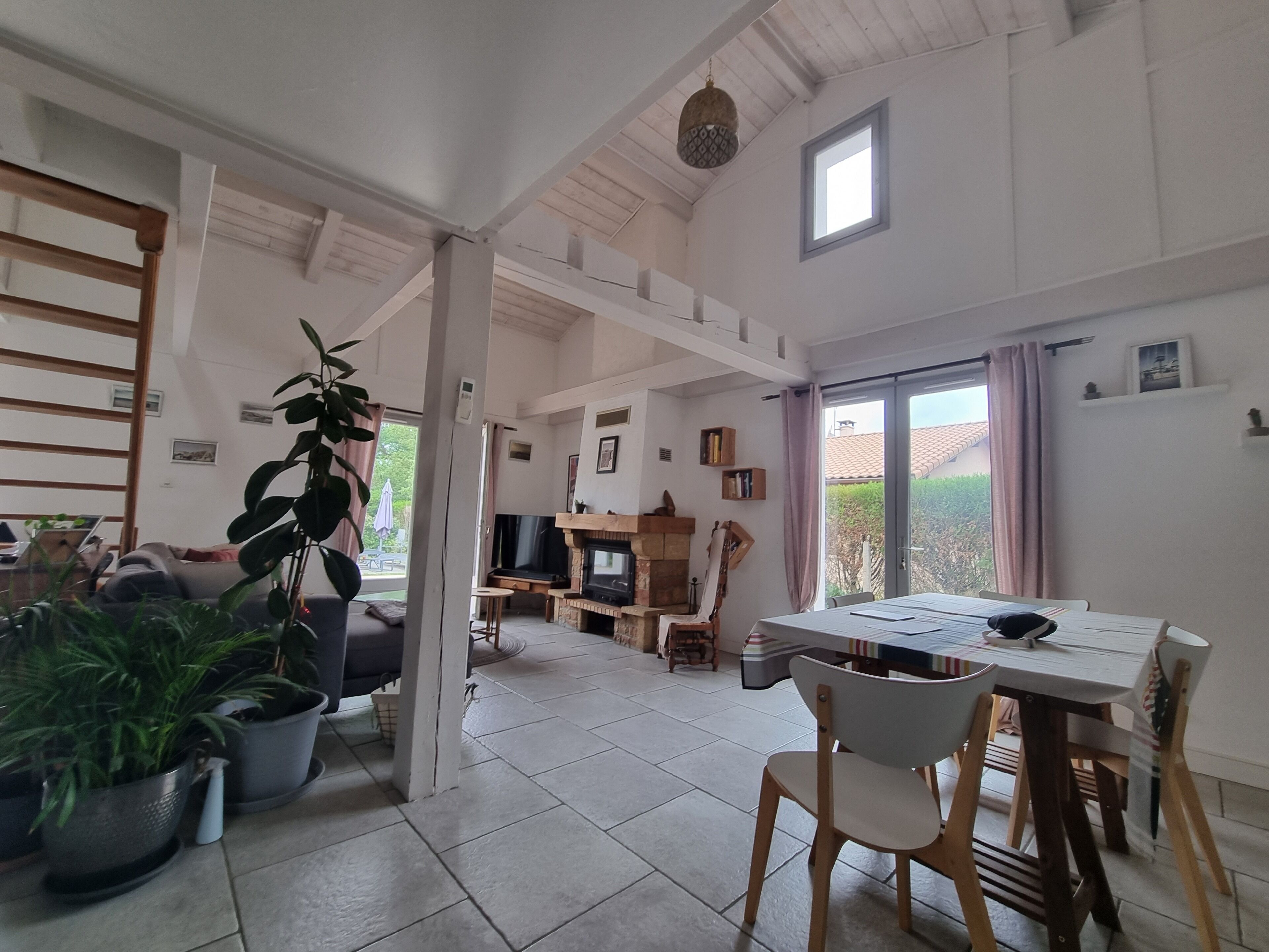 A spacious living area with a fireplace, a dining table, and several potted plants.
