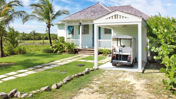 Ein bungalow mit überdachter Veranda, einem Golfwagen und einem Kiesweg zum Eingang.