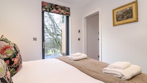 A bedroom with a bed, a window with a floral curtain, a door, and a framed picture on the wall. - Herdwick Cabin (Penrith)