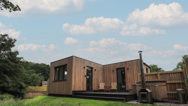 A modern wooden cabin with a small porch and two chairs. - Herdwick Cabin (Penrith)