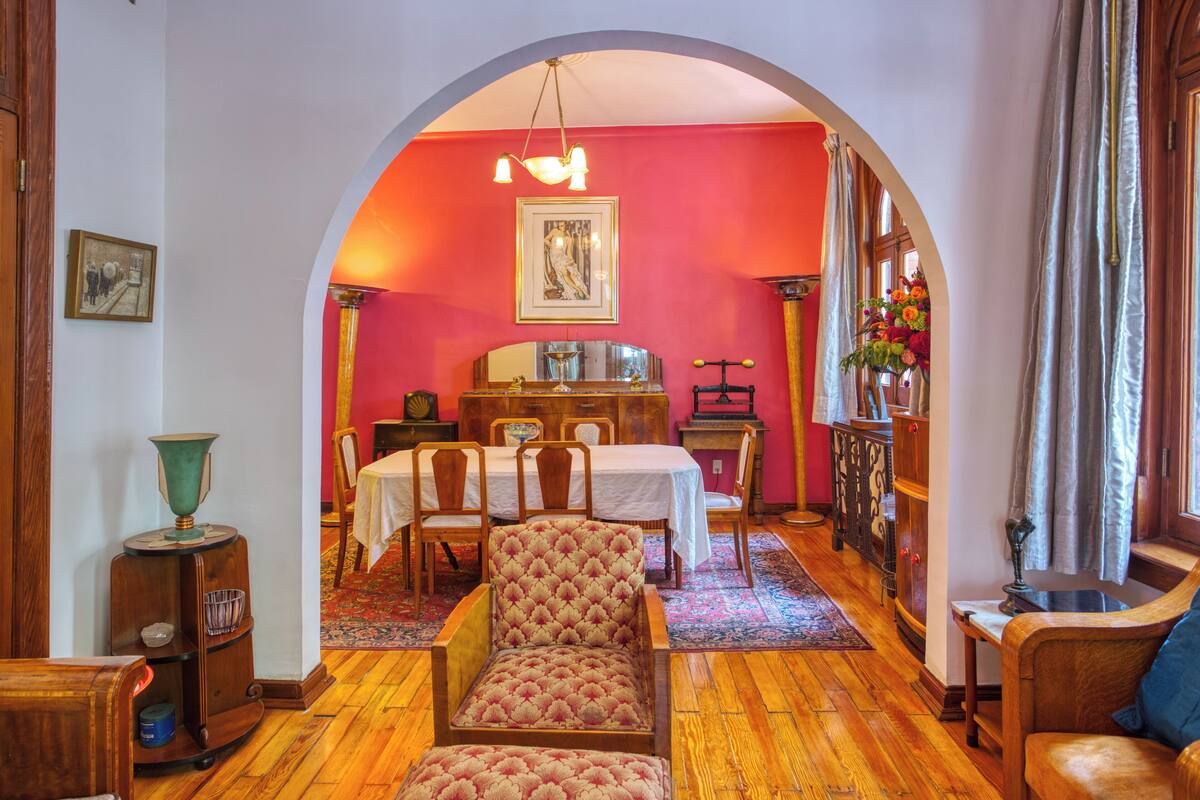 A room with a wooden floor, a dining table with chairs, a sofa, and a decorative lamp.