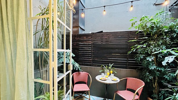 Un pequeño patio con dos sillas rojas, una mesa con una bebida y luces colgantes.