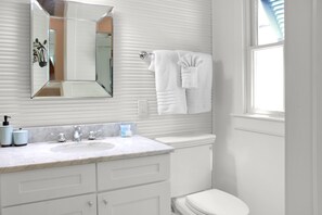 A bathroom with a white sink, mirror, and toilet. There is a towel hanging on the wall.
