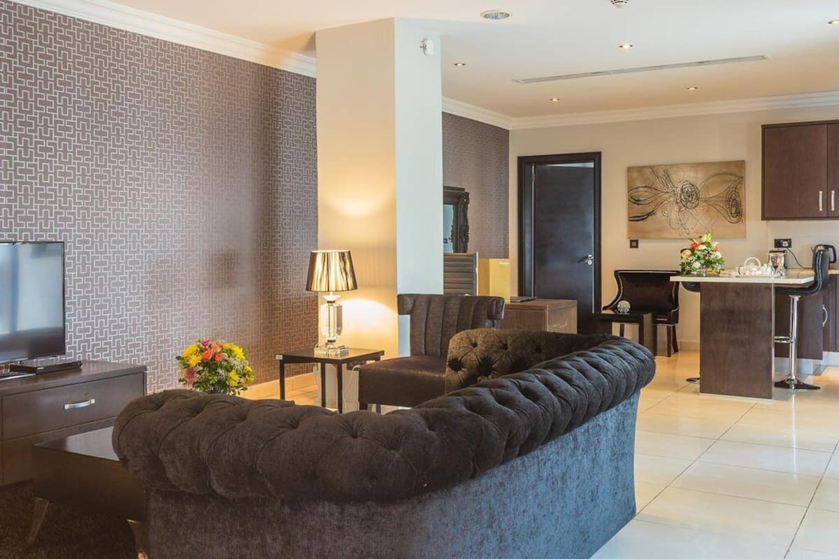 A modern living room with a large sectional sofa, a flat-screen TV, a small table with a lamp, and a decorative vase.