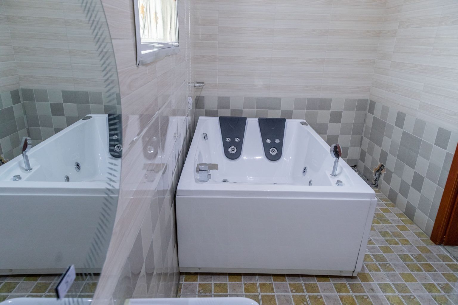 Two white freestanding tubs in a bathroom with tiled walls and floor.