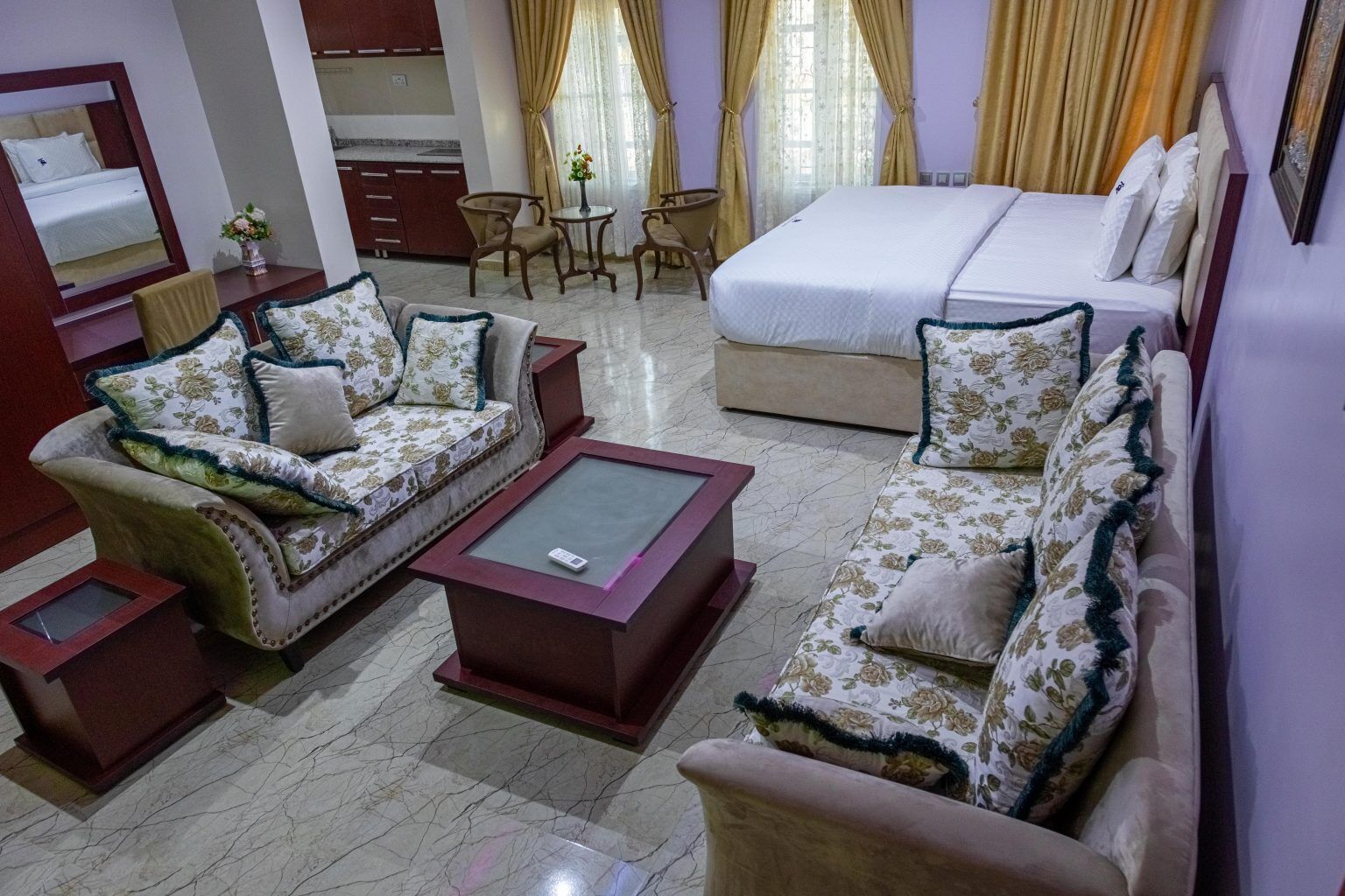Una habitación de hotel con cama, dos sofás, una mesa de centro, una mesa de comedor y una cocina.