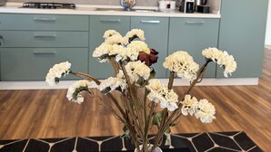 A modern kitchen with teal cabinets, a white vase with flowers on a black table, and a hexagonal patterned rug.