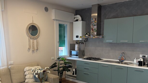 A modern kitchen with teal cabinets, a wooden dining table, and a built-in stove.