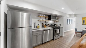 A modern kitchen with stainless steel appliances, a microwave, and wooden shelves.